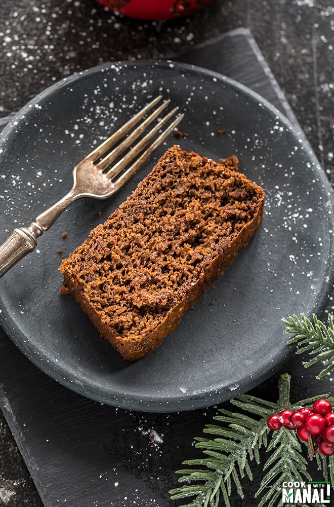 sliced of vegan gingerbread cake in a round black plate with a fork and festive decor on the side