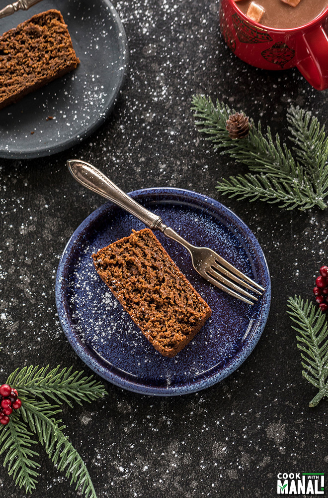 slice of vegan gingerbread cake in a blue plate with a fork and festive decor on the sides