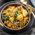 instant pot aloo baingan served in a small copper kadai, garnished with cilantro and spoons and napkin on the side
