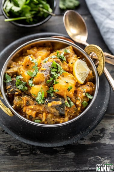 instant pot aloo baingan served in a small copper kadai, garnished with cilantro and spoons and napkin on the side