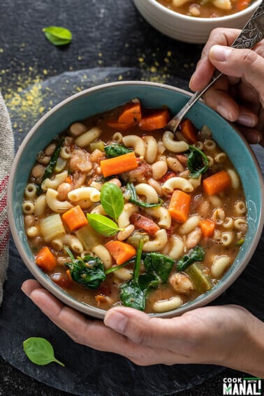 pair of hands holding a soup into a bowl of minestrone soup