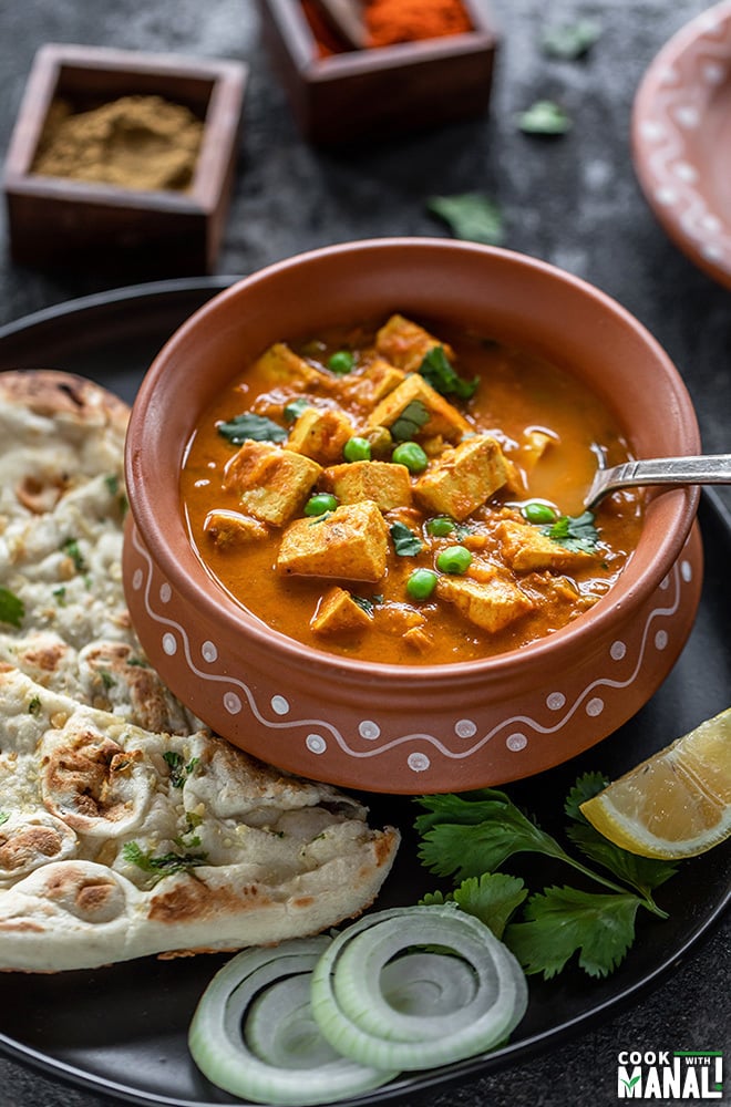 tofu matar in a clay pot with a spoon, served with naan on the side