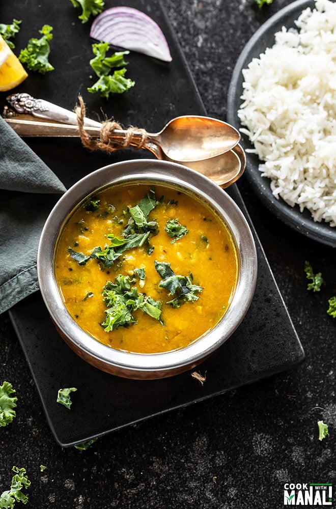 kale garlic dal in a copper bowl with spoon in the background and a plate of white rice on the side
