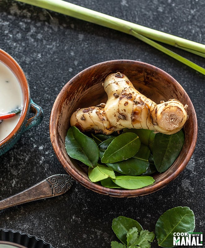 galangal and kaffir lime leaves in a bowl with stalk of lemongrass in the background