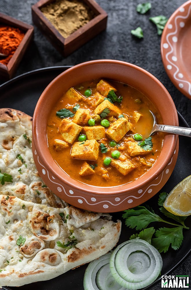 tofu matar in a clay pot with a spoon, served with naan on the side