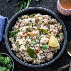 bowl of upma with glass of chai on one side, blue color kitchen towel on another side and curry leaves in the background