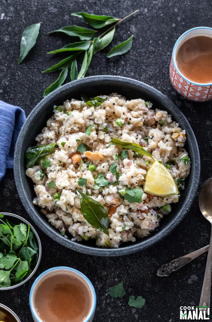 bowl of upma with glass of chai on one side, blue color kitchen towel on another side and curry leaves in the background