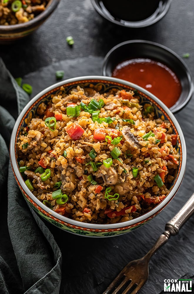 bowl of vegan cauliflower fried rice with a napkin on the side and bowls filled with sauces in the background