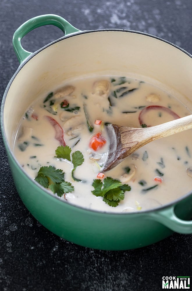 vegan tom kha gai soup in a green pot with a ladle