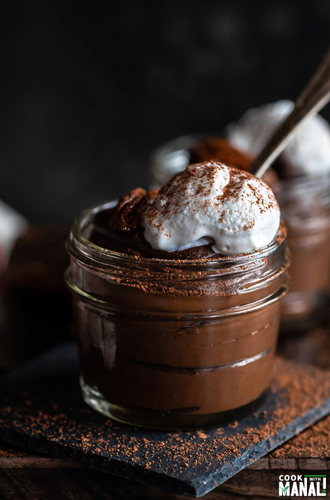 jar of chocolate avocado pudding topped with coconut whipped cream and a spoon on the side
