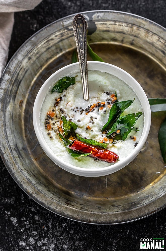 bowl of coconut chutney tempered with curry leaves, mustard seeds, dried red chilies and served with a spoon