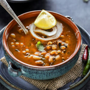 black eyed pea curry in a blue bowl with a lemon wedge and a ring of onion