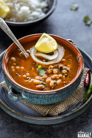 black eyed pea curry in a blue bowl with a lemon wedge and a ring of onion