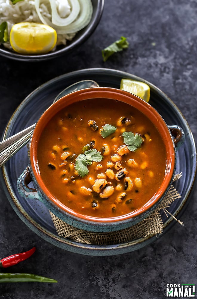 black eyed pea curry in a blue bowl with two spoons and lemon wedge in the background