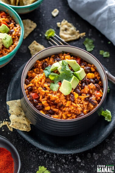 enchilada rice in a black bowl topped with avocados with a side of tortilla chips