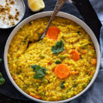 bowl of quinoa khichdi with a spoon with a small bowl of yogurt and lemon slice in the background