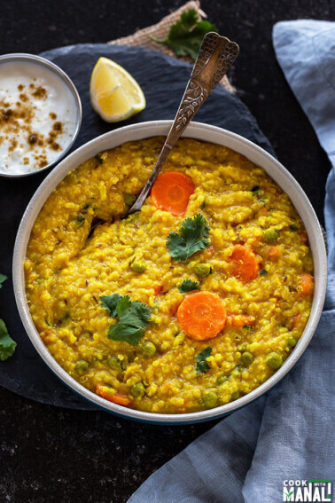 bowl of quinoa khichdi with a spoon with a small bowl of yogurt and lemon slice in the background