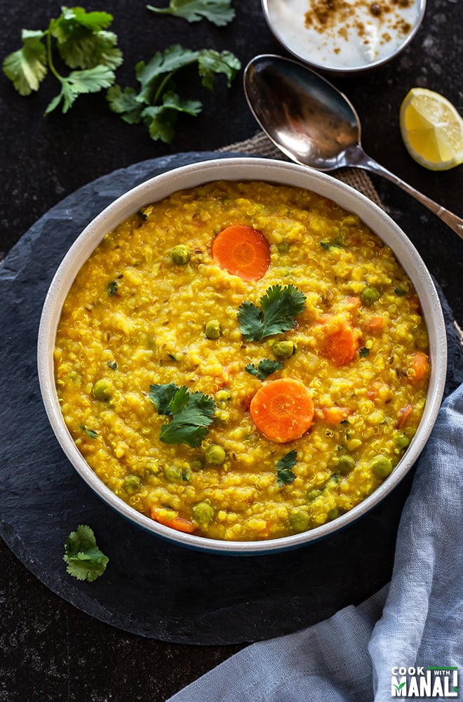 bowl of quinoa khichdi with a spoon in the background along with a bowl of yogurt and some cilantro