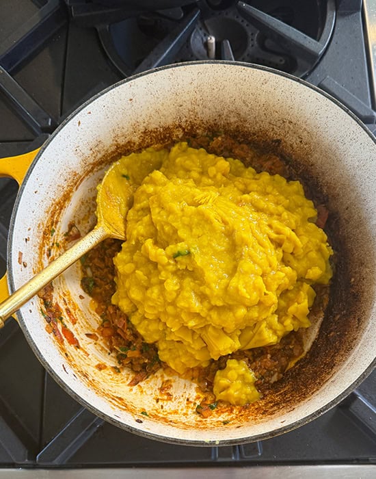 dal being added to pot of cooked masala in a pot