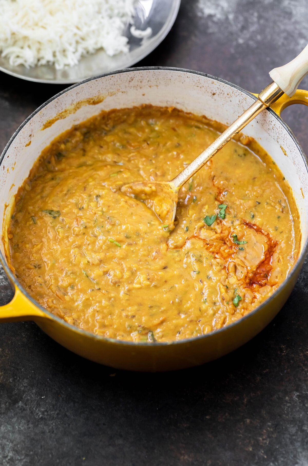 dal tadka in a yellow pot with a spoon on side