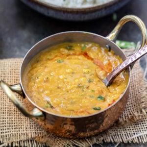 dal tadka served in a copper kadai with a spoon and a bowl of rice in the background