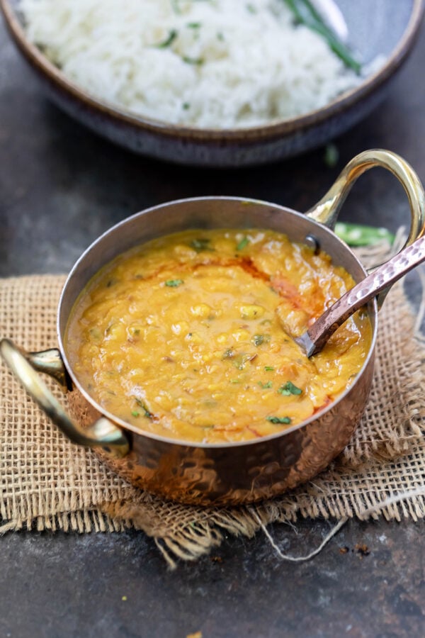 dal tadka served in a copper kadai with a spoon and a bowl of rice in the background
