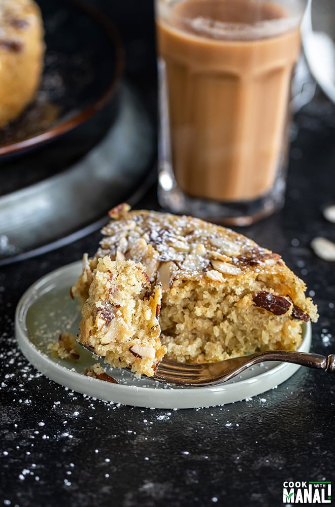 slice of almond cardamom cake in a round plate with a glass of chai in the background