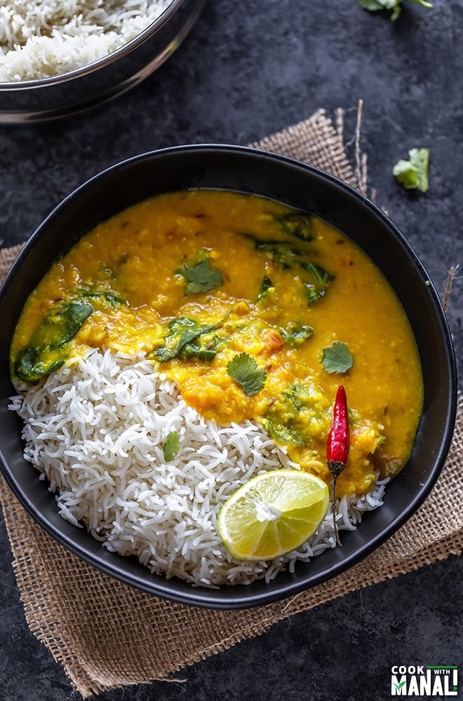 dal and rice in a black bowl with a red chili and lime wedge