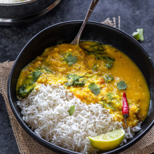 rice and dal in a black bowl with a red chili and a spoon