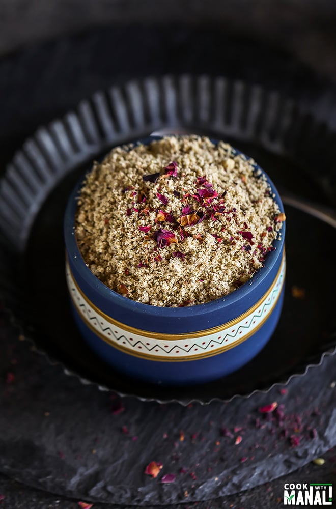 thandai masala powder in a blue bowl sprinkled with dried rose petals on top