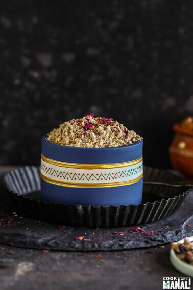 thandai powder in a blue color bowl with rose petals scattered on the sides