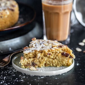 slice of almond cardamom cake in a round plate with a glass of chai in the background