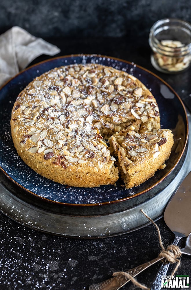 vegan almond cardamom cake in a round blue plate with a slice of cake removed from the side