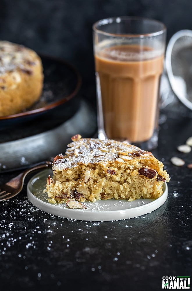 slice of almond cardamom cake in a round plate with a glass of chai in the background