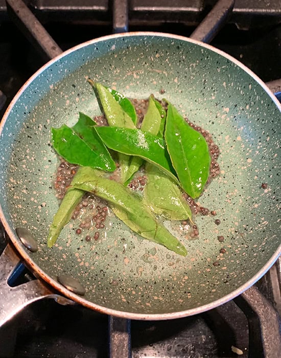 curry leaves with mustard seeds in a small tadka pan