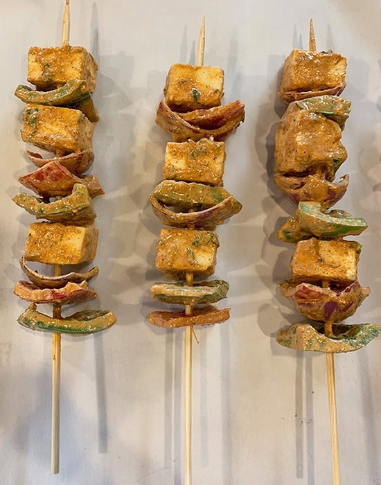 paneer tikka arranged on wooden skewers