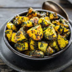 aloo methi in a black bowl with a spoon on the side