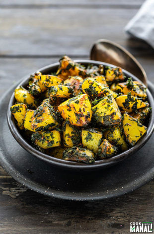 aloo methi in a black bowl with a spoon on the side