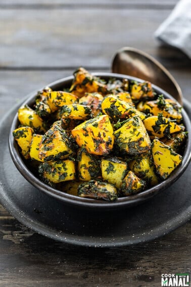 aloo methi in a black bowl with a spoon on the side