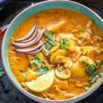 Aloo Mushroom Masala served in a bowl garnished with sliced onions, lemon wedge and cilantro