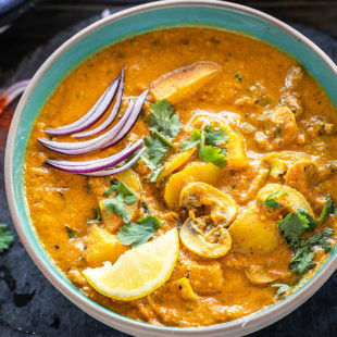 Aloo Mushroom Masala served in a bowl garnished with sliced onions, lemon wedge and cilantro