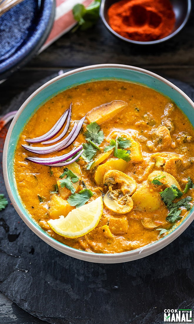 Aloo Mushroom Masala served in a bowl garnished with sliced onions, lemon wedge and cilantro