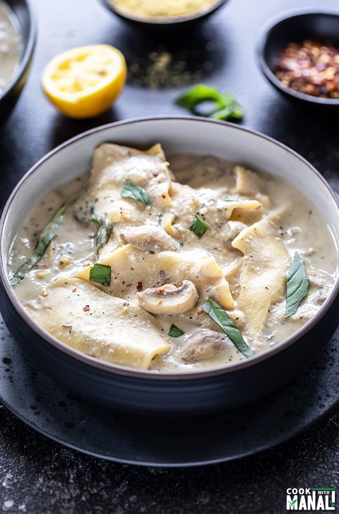 white lasagna soup served in a black bowl, garnished with basil with more basil and squeezed lemon in the background