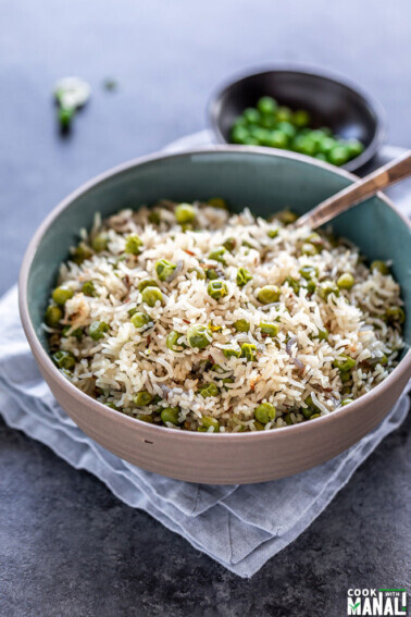 bowl of matar pulao with spoon placed on a blue napkin