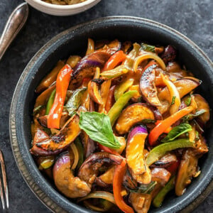 thai basil eggplant served in a black bowl with a small bowl of rice in the background