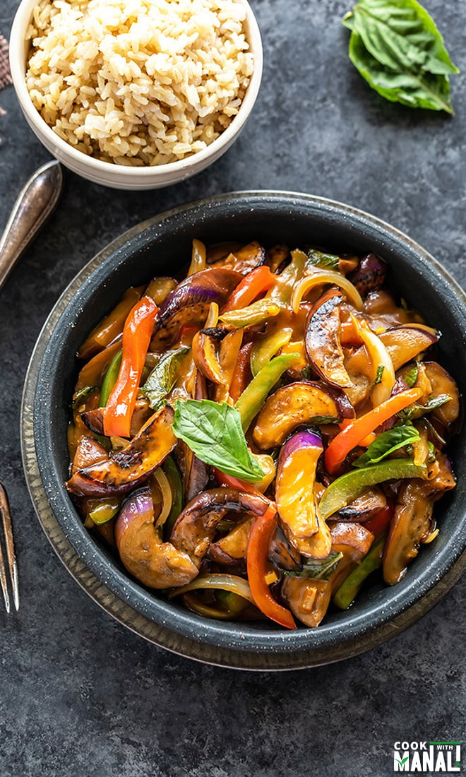 thai basil eggplant served in a black bowl with a small bowl of rice in the background