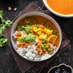 shot of vegan makhani sauce with cauliflower and green peas served over white rice and garnished with cilantro.