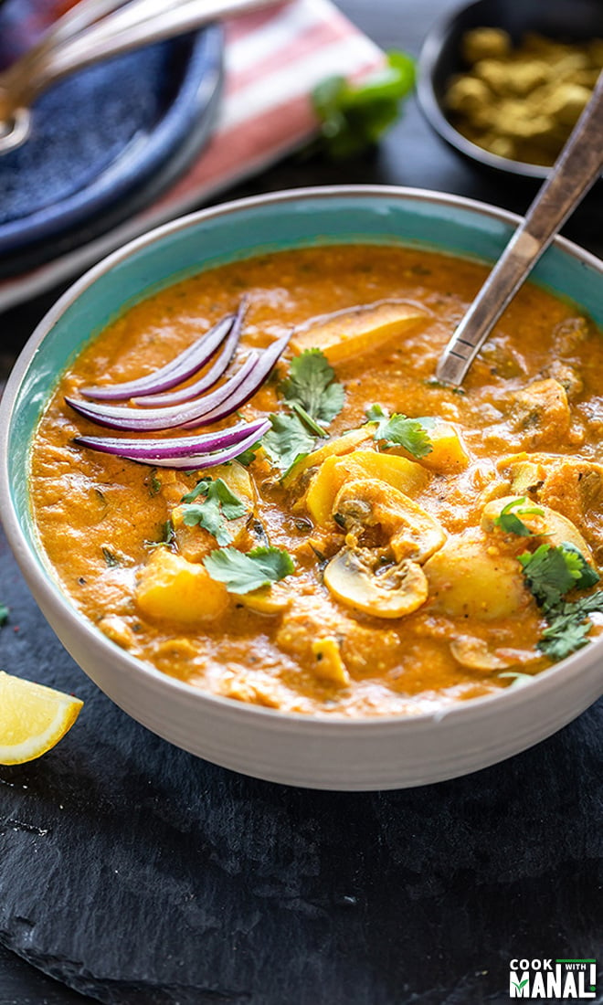 Aloo Mushroom Masala served in a bowl with a spoon and garnished with sliced onion and chopped cilantro