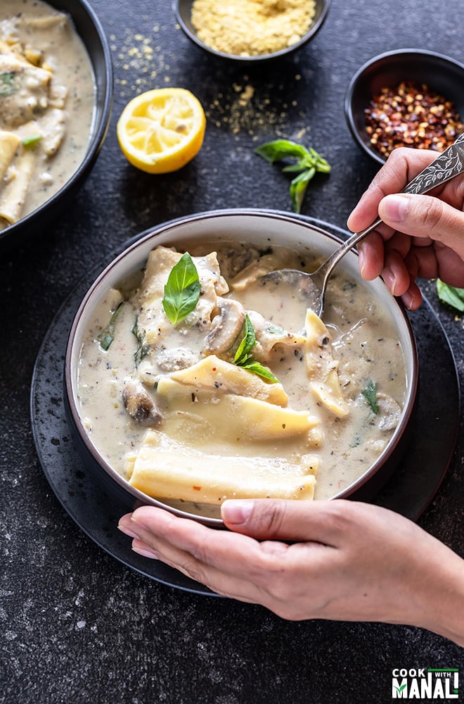 pair of hands holding a bowl of vegan mushroom white lasagna soup with some basil and squeezed piece of lemon in the background