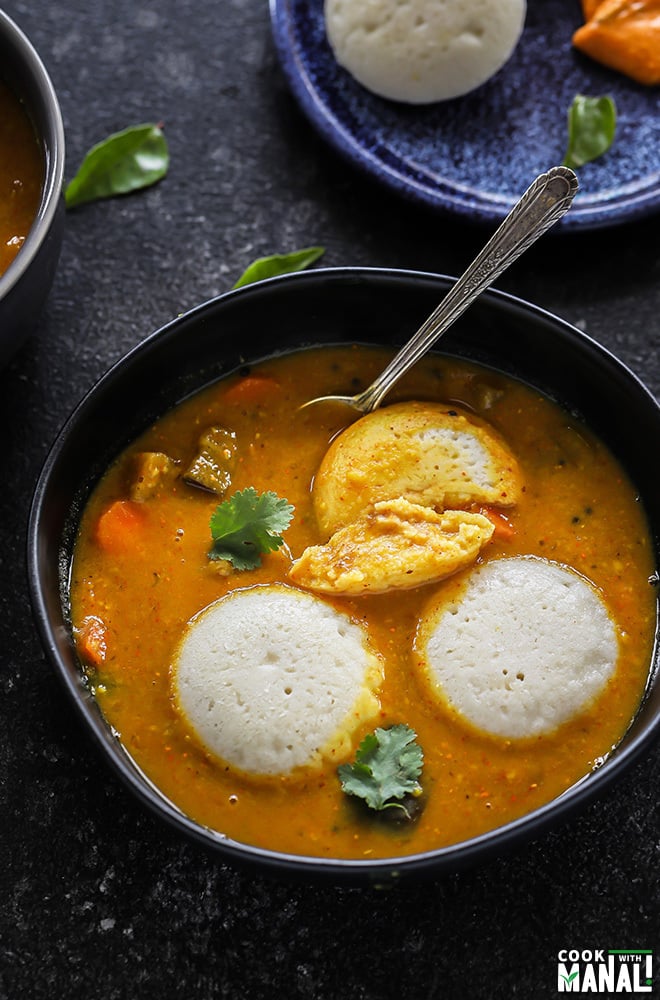 3 pieces of idli served with sambar in a black bowl